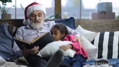 带着圣诞老人帽子，留着灰白胡子的爷爷<strong>正在</strong>给他那昏昏欲睡的可爱的混血儿孙女读书